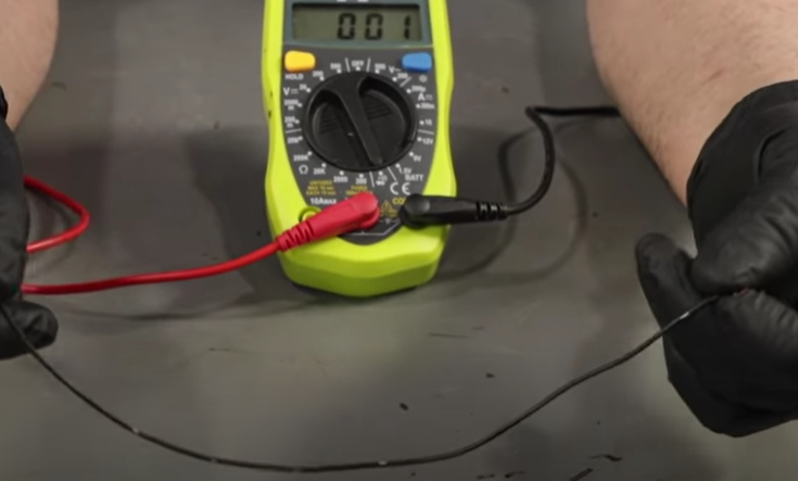 Placing two leads from a digital multimeter to test for continuity on an electrical wire