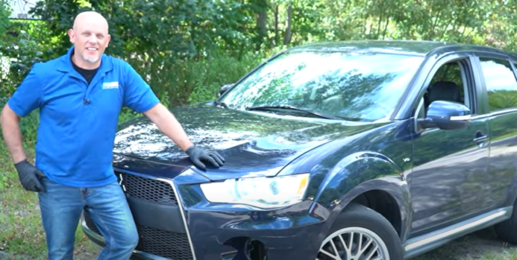 Mechanic standing in front of a 2007 to 2013 Mitsubishi Outlander, reviewing the top problems with the 2nd generation