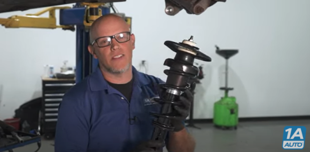 1A Auto mechanic holding a strut while reviewing the symptoms of bad struts and what to do if you have a strut with a broken coil spring