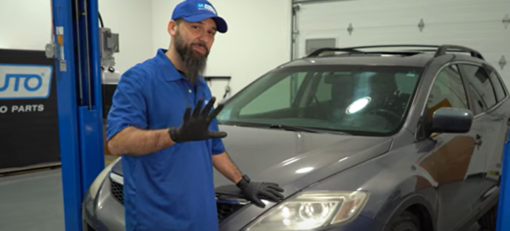 Mechanic standing in front of a 1st gen 2007 to 2015 Mazda CX-9 and reviewing its most common top 5 problems